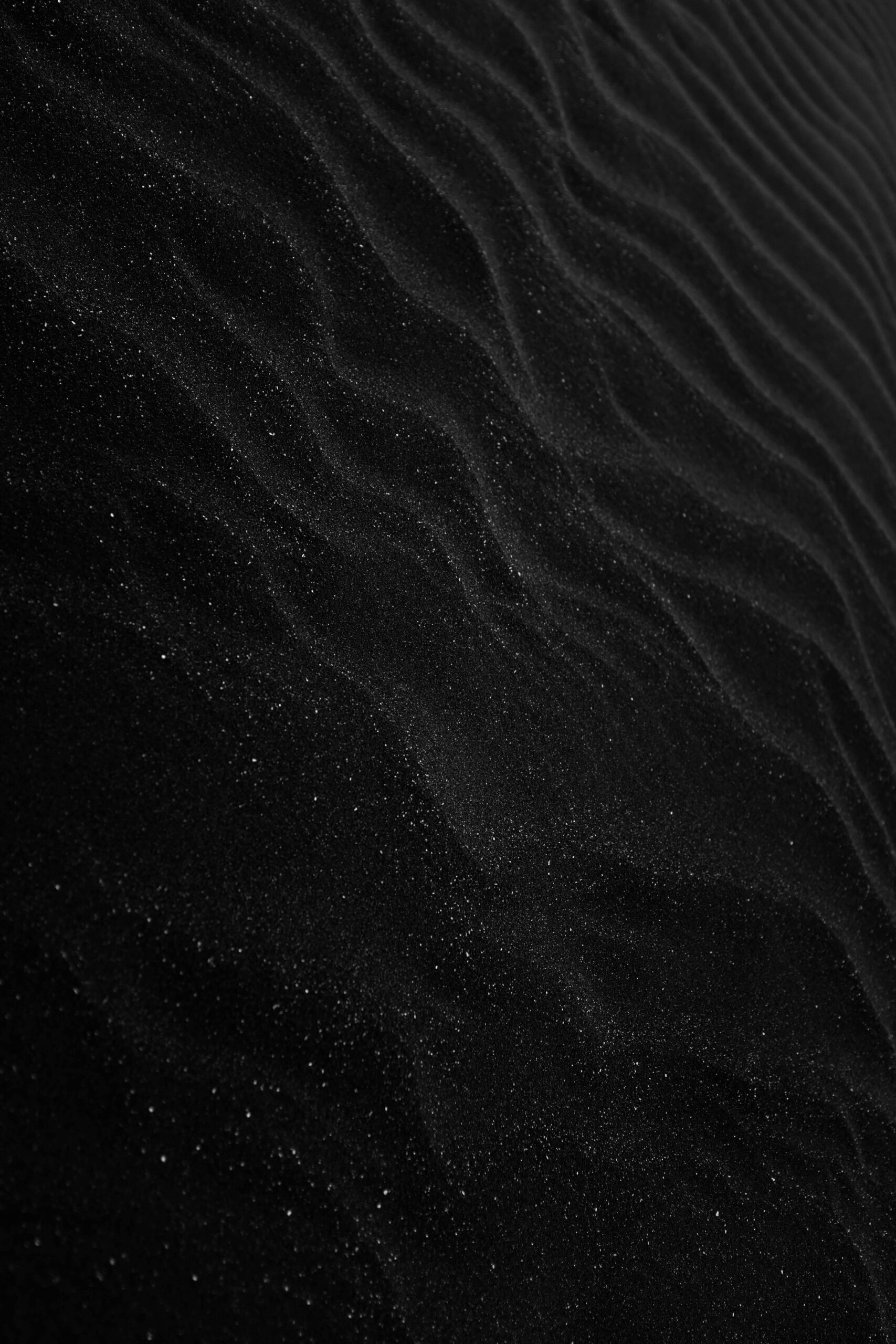 Textured black sand with ripples resembling dunes, creating a dark, abstract aesthetic.